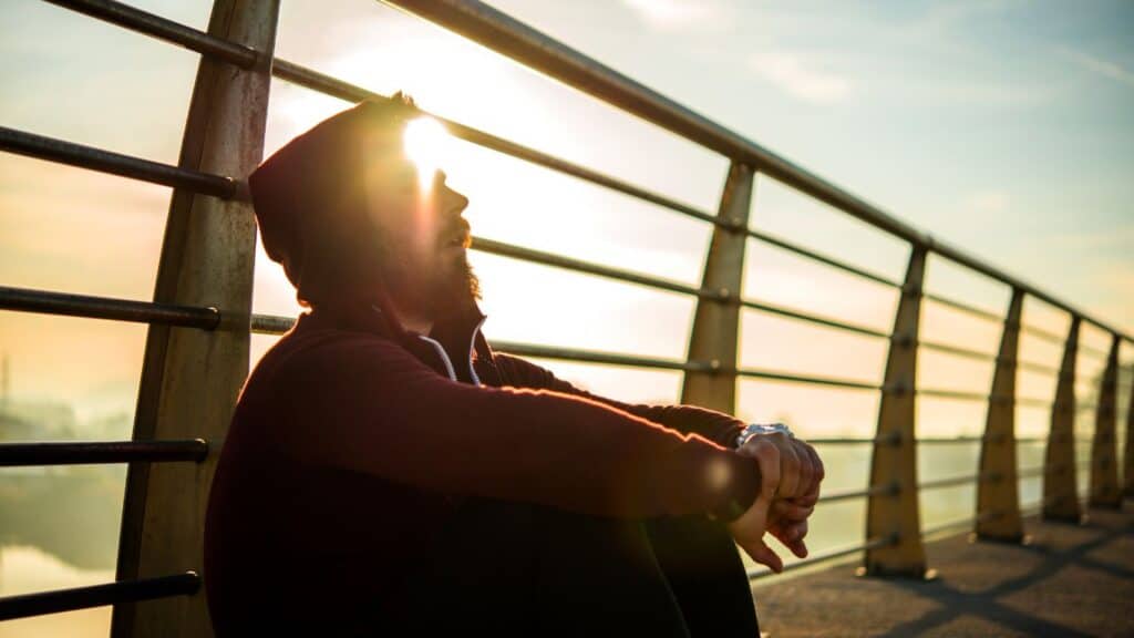 Man sitting against fence with sun setting behind himn