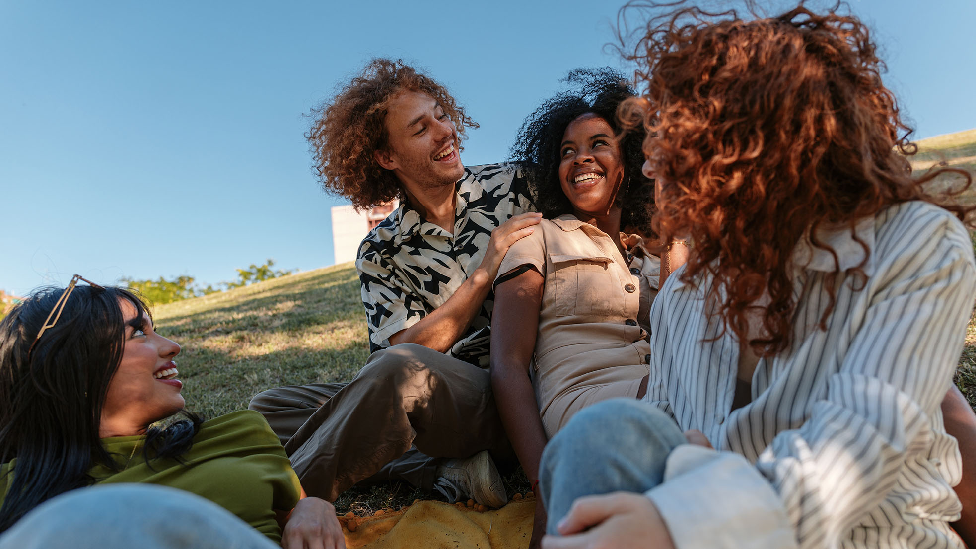 Group of happy young adults relaxing together on a blanket in a park, enjoying conversation and laughter on a sunny day