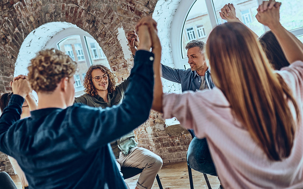Young people celebrating recovery from alcohol addiction, team work of anonymous addicts club, raised hands up together. Selective focus