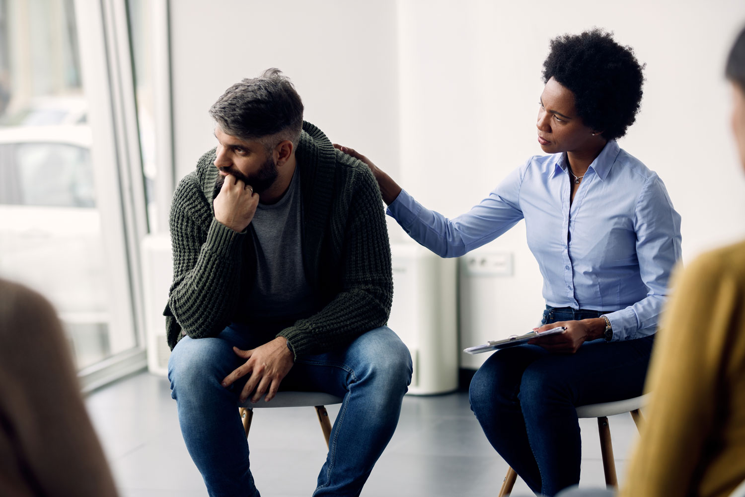 Female clinician sitting with hand on shoulder of male client